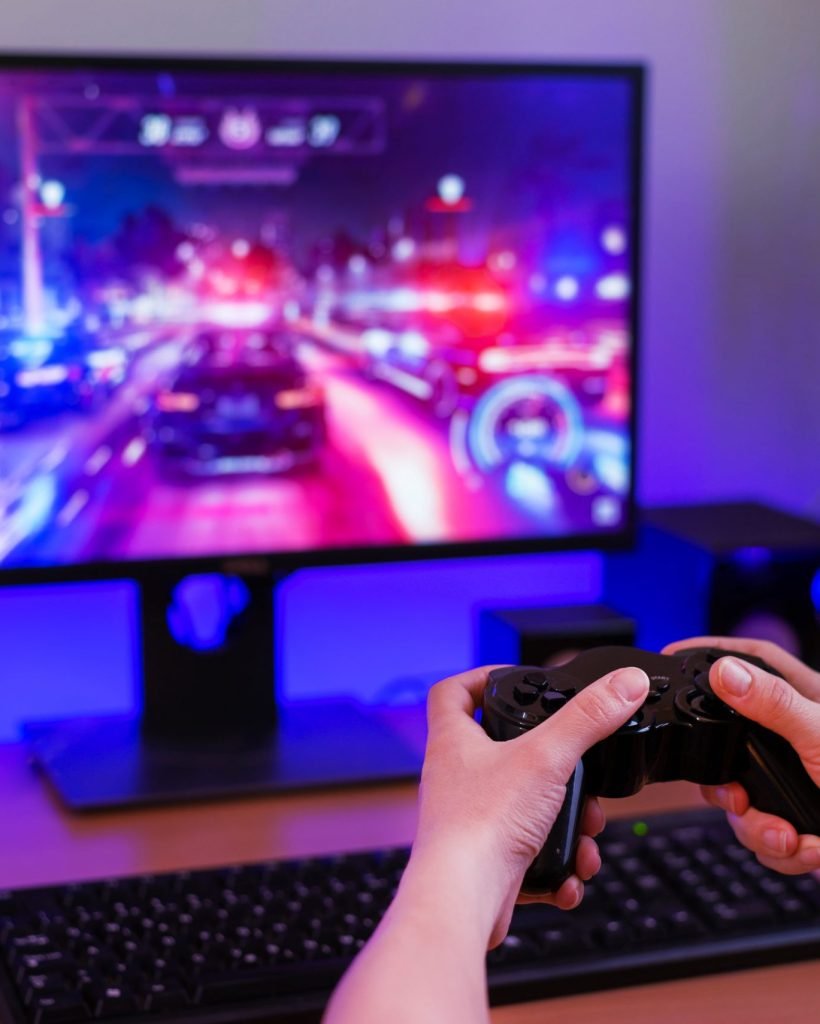 playing-racing-games-computer-concept-hand-holds-joystick-background-is-gaming-computer-with-rgb-light-min-scaled